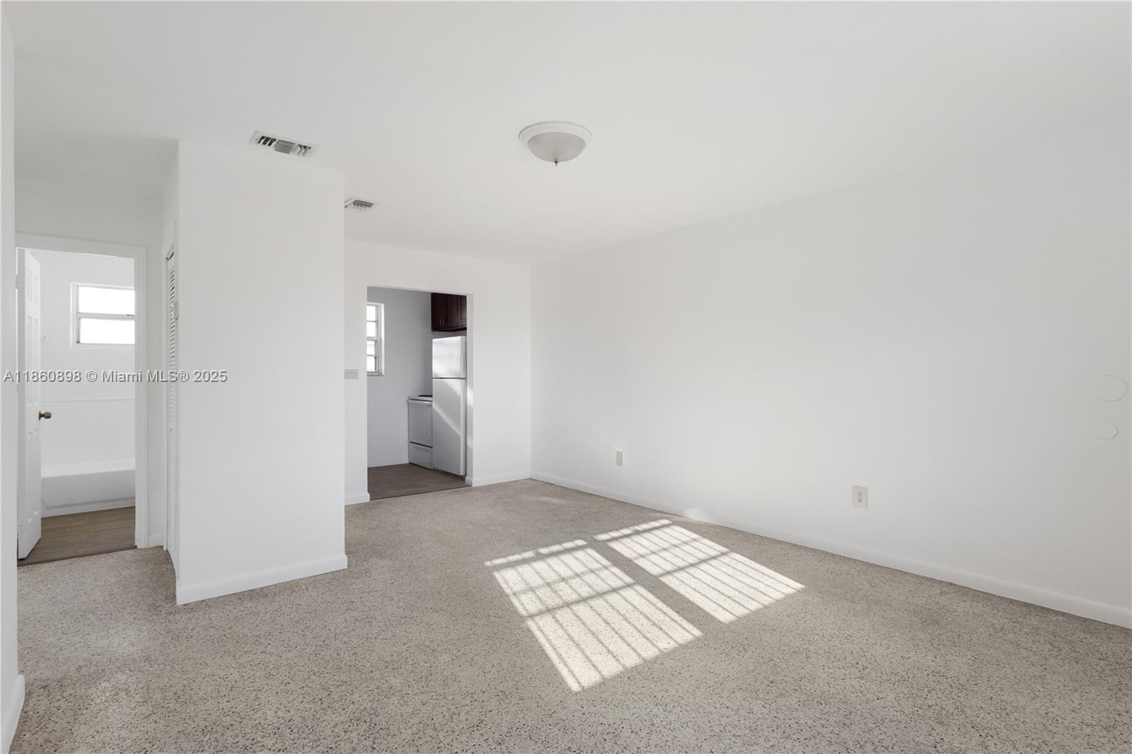 An empty room with beige carpet, white walls, and a doorway leading to a kitchen — 1251 NW 59th St # 3, Miami FL 33142, MIAMI, FL