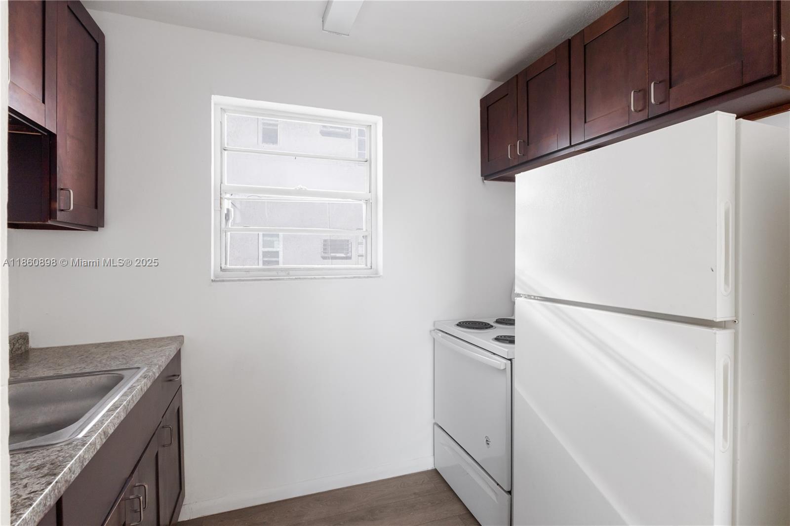 A small kitchen features dark wood cabinets, white appliances, and a window above the floor — 1251 NW 59th St # 3, Miami FL 33142, MIAMI, FL
