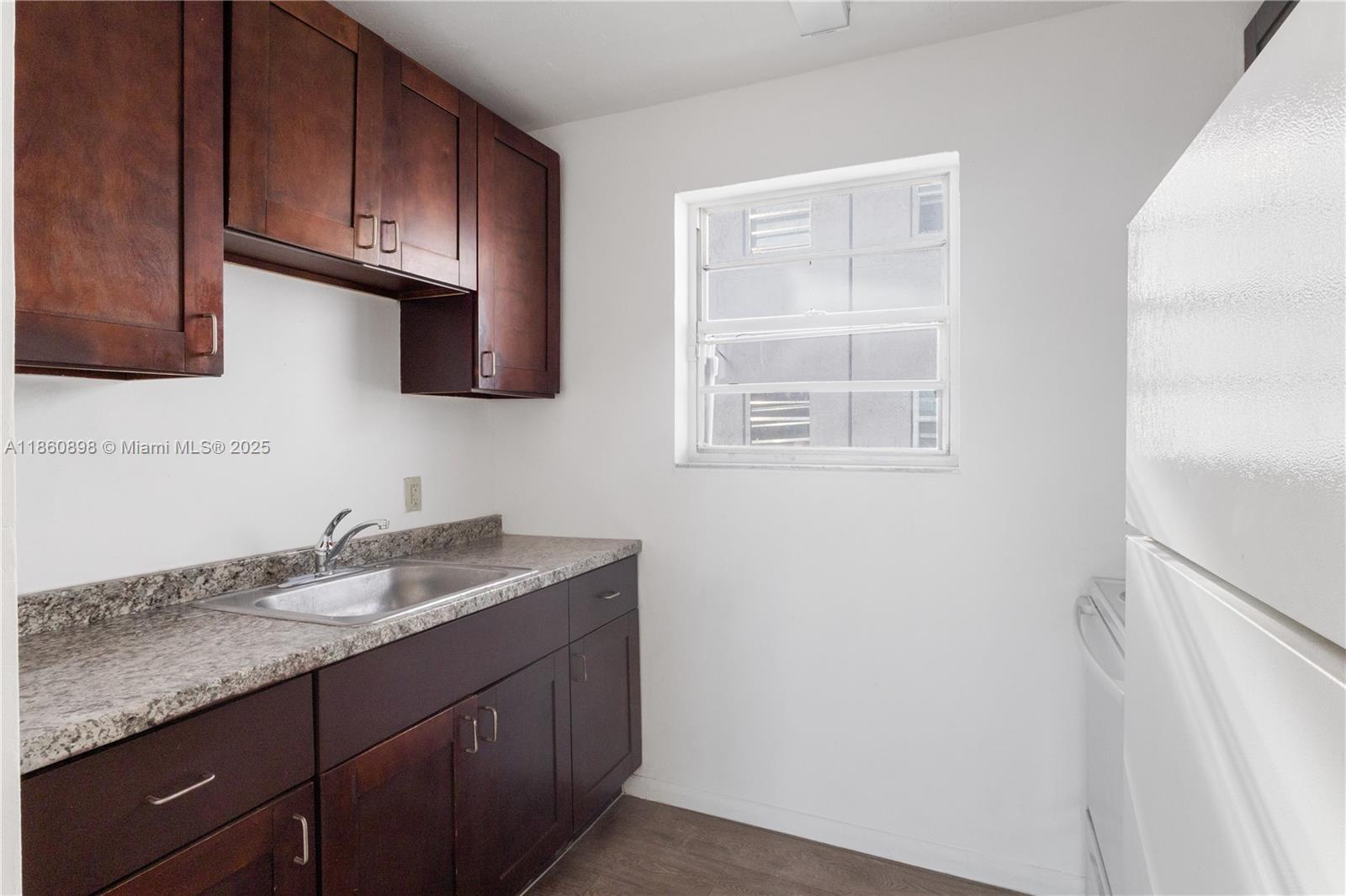 A small kitchen features dark wood cabinets, a granite countertop, a stainless steel sink, and a window — 1251 NW 59th St # 3, Miami FL 33142, MIAMI, FL
