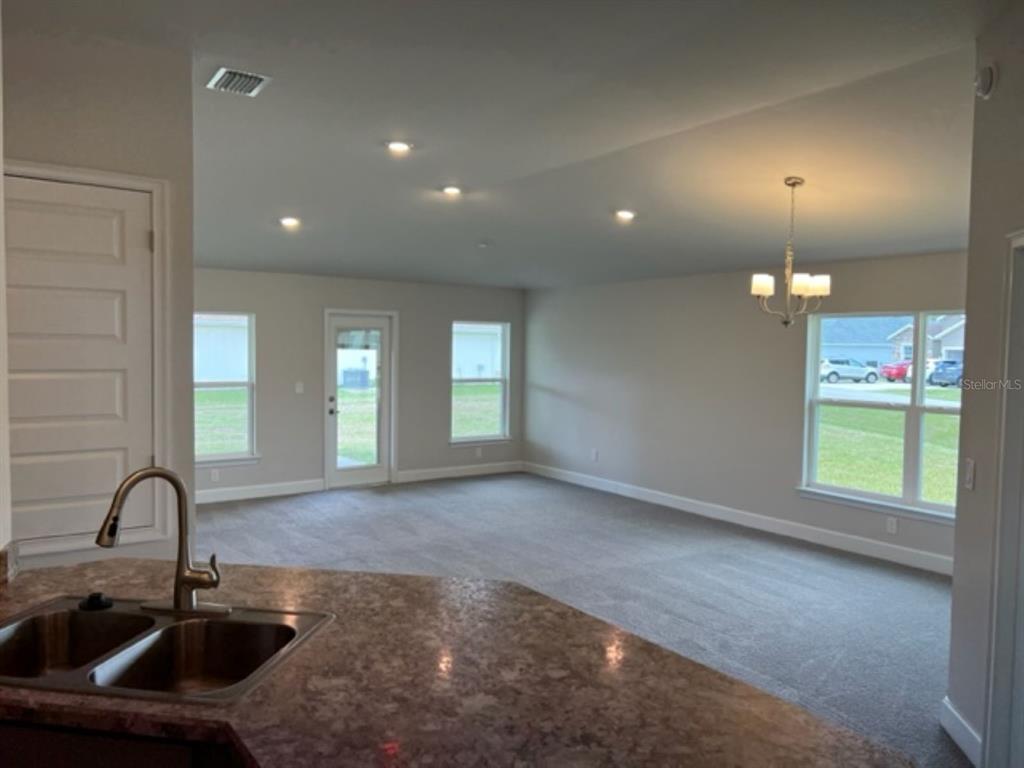 A kitchen sink overlooks an open-concept living area with carpeted flooring and a dining chandelier — 2206 NW 23RD LOOP, OCALA, FL