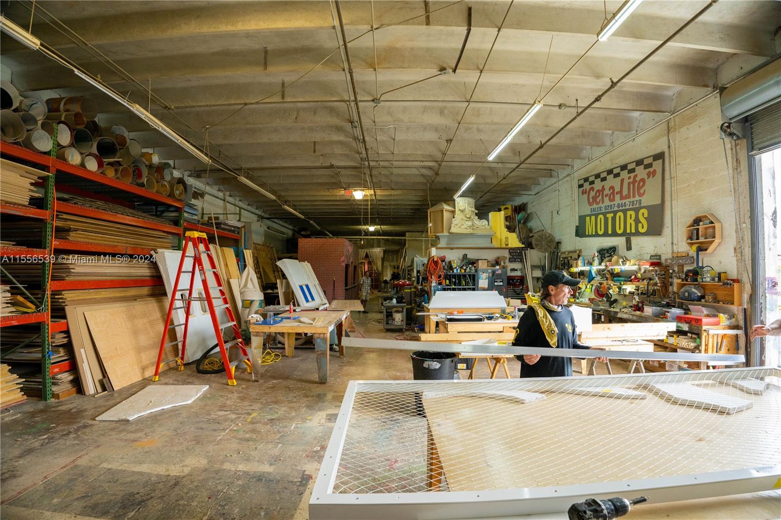 A spacious, cluttered workshop features exposed ceilings, industrial lighting, storage racks, and a workbench area — 1240 NW 74th St, Miami FL 33147, MIAMI, FL