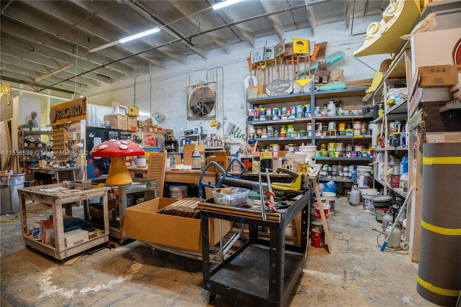 A cluttered workshop space features industrial shelving, paint supplies, work tables, and various props — 1240 NW 74th St, Miami FL 33147, MIAMI, FL