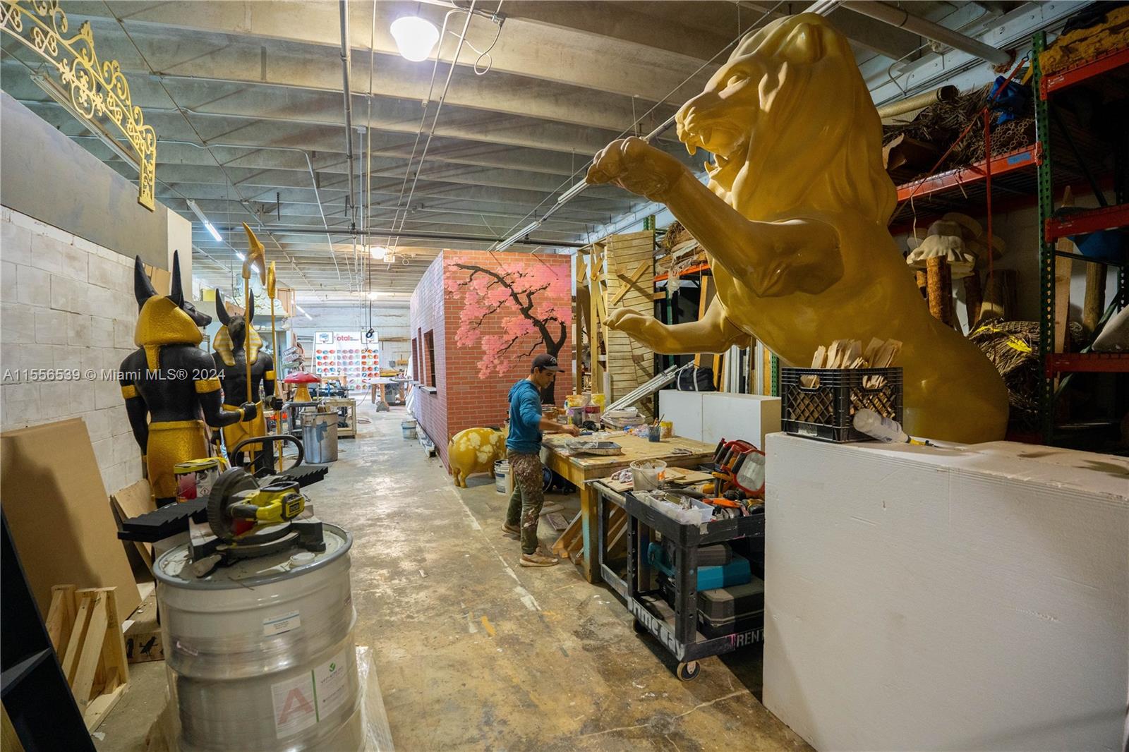 A person works in a cluttered workshop filled with large decorative sculptures and props — 1240 NW 74th St, Miami FL 33147, MIAMI, FL