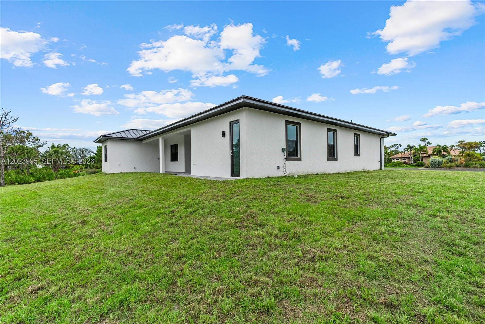 The exterior of a modern, white, single-story house sits on a large, grassy lot — 12526 Indian Shell Trail, Bokeelia FL 33922, BOKEELIA, FL