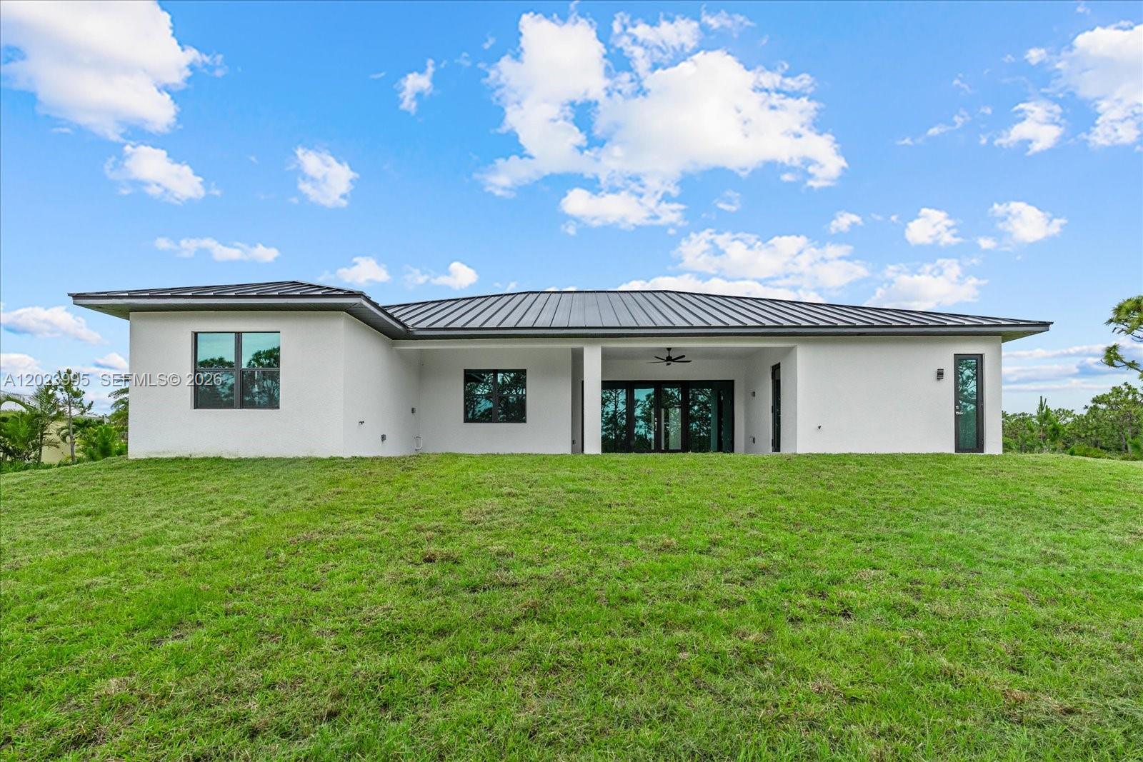 The exterior of a modern white house features a dark metal roof and a covered patio — 12526 Indian Shell Trail, Bokeelia FL 33922, BOKEELIA, FL