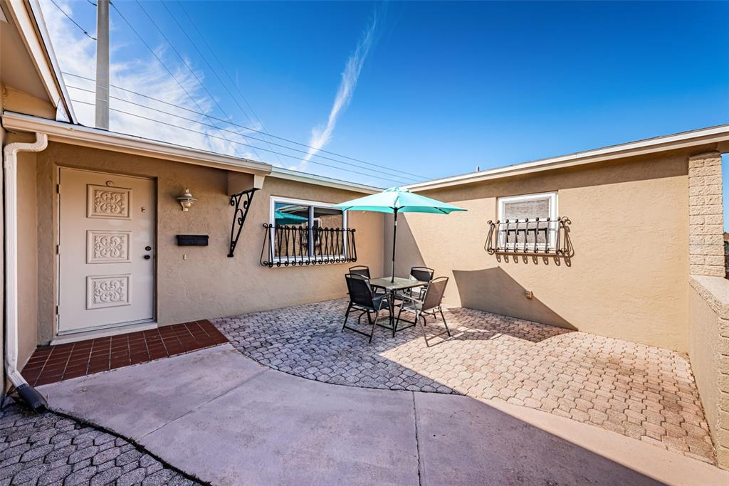 A paved patio area features a small dining set with a turquoise umbrella and windows — 4106 53RD AVENUE S, ST PETERSBURG, FL