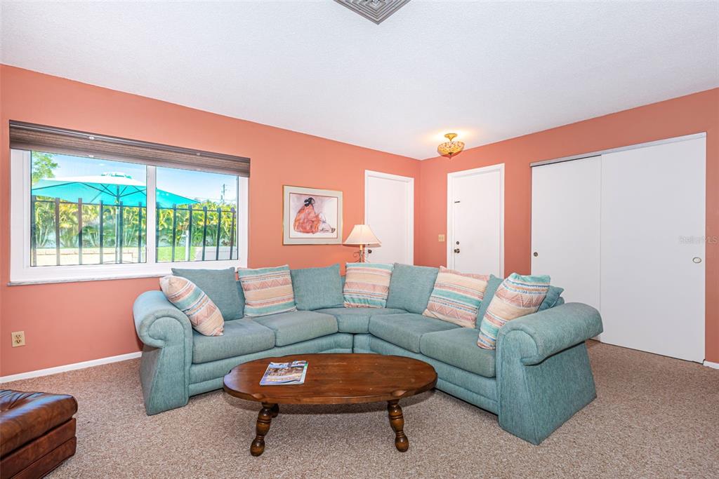 A living room features a teal sectional sofa, a wooden coffee table, and coral walls — 4106 53RD AVENUE S, ST PETERSBURG, FL