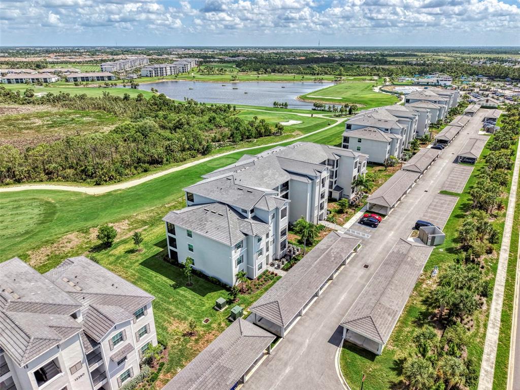 An aerial view shows multi-story apartment buildings with covered parking lots near a golf course — 12240 WELLEN GOLF STREET UNIT 304, VENICE, FL