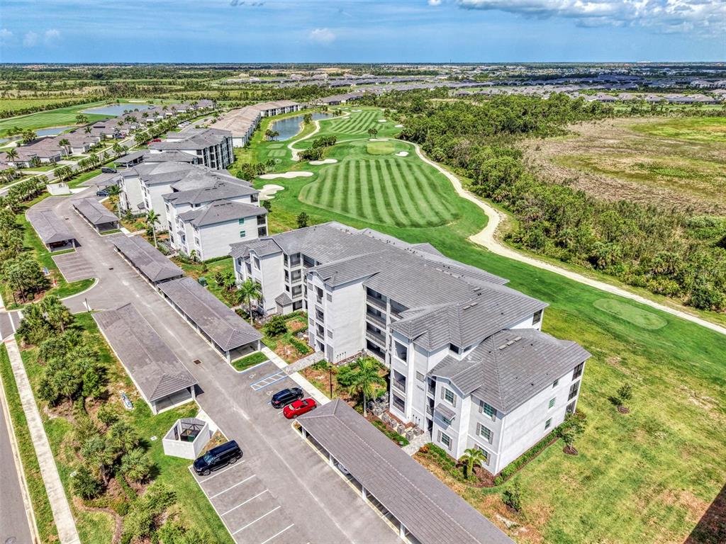 An aerial view shows multi-story apartment buildings with covered parking adjacent to a golf course — 12240 WELLEN GOLF STREET UNIT 304, VENICE, FL
