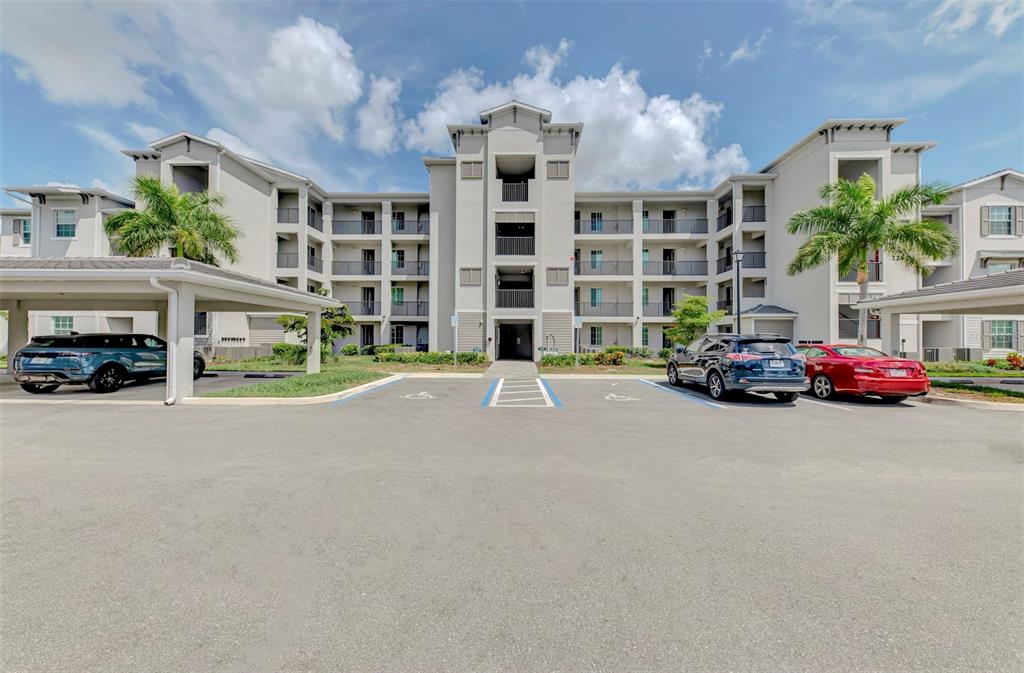A multi-story apartment building exterior features a central entrance, covered parking, and a paved lot — 12240 WELLEN GOLF STREET UNIT 304, VENICE, FL