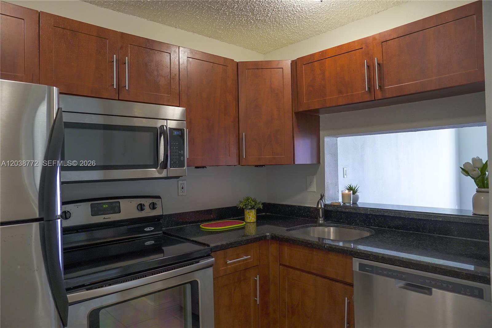 A kitchen features wood cabinets, stainless steel appliances, and dark granite countertops — 482 NW 165th St Rd # A504, Miami FL 33169, MIAMI, FL