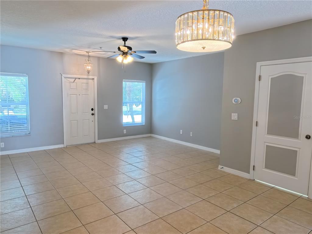 An open living area features tile flooring, gray walls, a ceiling fan, and two chandeliers — 13349 HARBOR SHORE LANE, WINTER GARDEN, FL