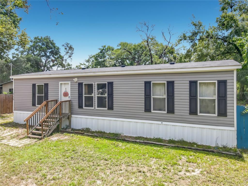 A single-story manufactured home with grey siding, black shutters, and a wooden staircase — 40628 PALM DRIVE, EUSTIS, FL