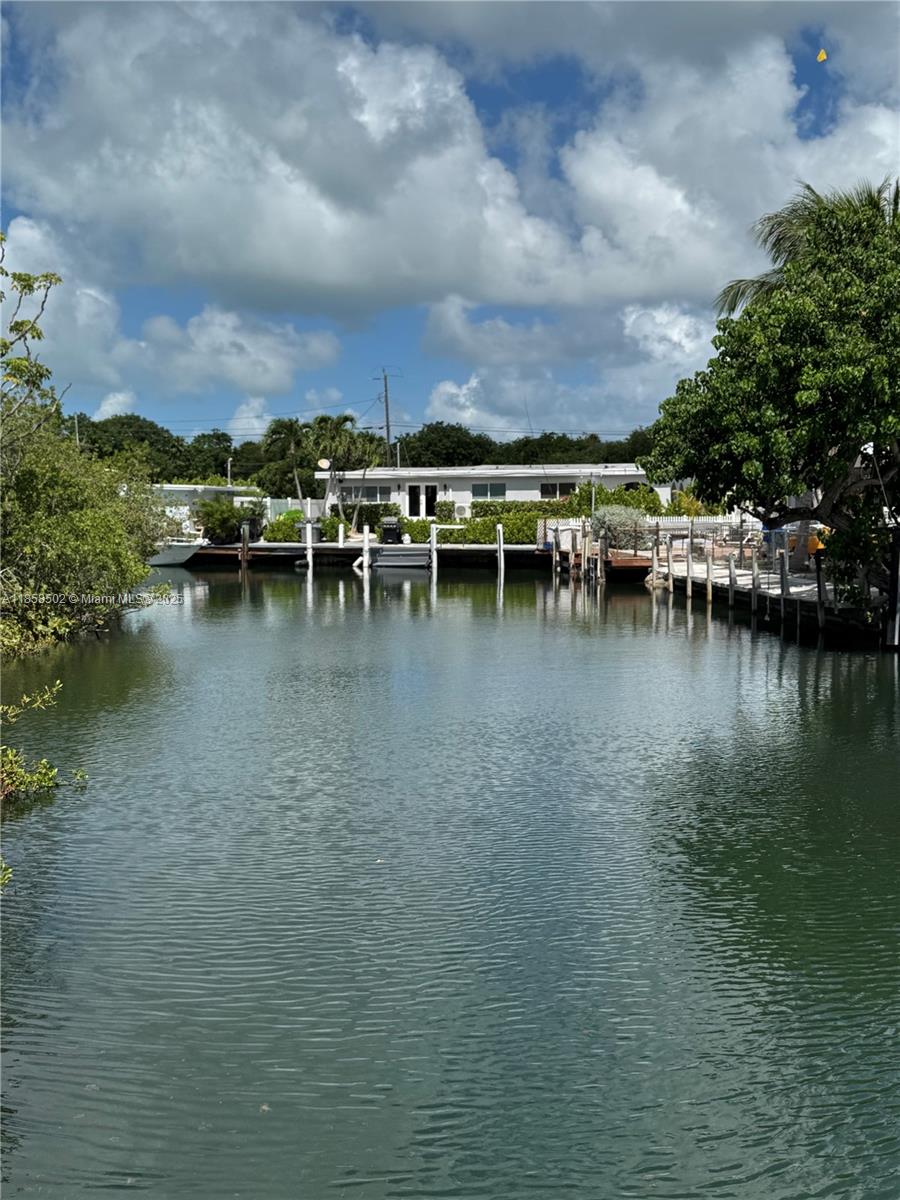 A canal view shows a white house with a wooden dock and lush surrounding trees — 1301 Grouper Dr # A, Marathon FL 33050, MARATHON, FL
