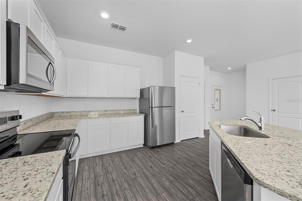 A kitchen features white cabinets, granite countertops, stainless steel appliances, and wood-look flooring — 572 BAY LEAF DRIVE, POINCIANA, FL
