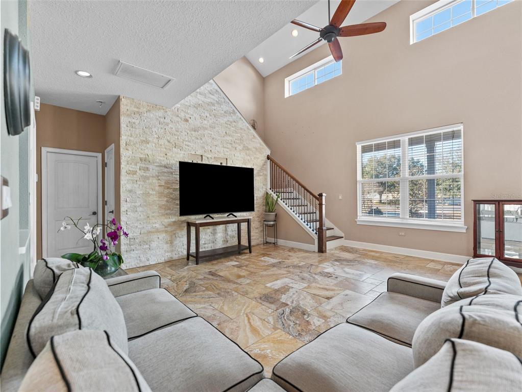 A living room features a stone accent wall, tile flooring, and stairs under a vaulted ceiling — 4702 CYPRESS SERENITY DRIVE, PLANT CITY, FL