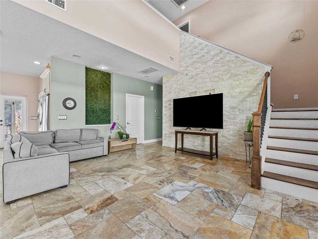 A living room features a stone accent wall with a television and tile flooring — 4702 CYPRESS SERENITY DRIVE, PLANT CITY, FL