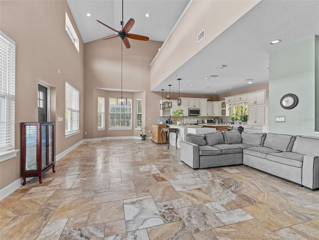 An open-concept living room and kitchen feature vaulted ceilings, tile flooring, and a sectional sofa — 4702 CYPRESS SERENITY DRIVE, PLANT CITY, FL