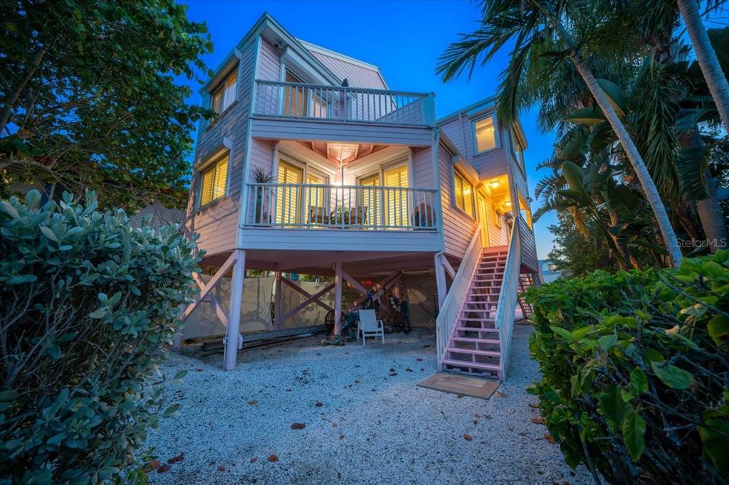 A pink elevated stilt house with two levels of balconies and an outdoor staircase — 20051 GULF BOULEVARD, INDIAN SHORES, FL
