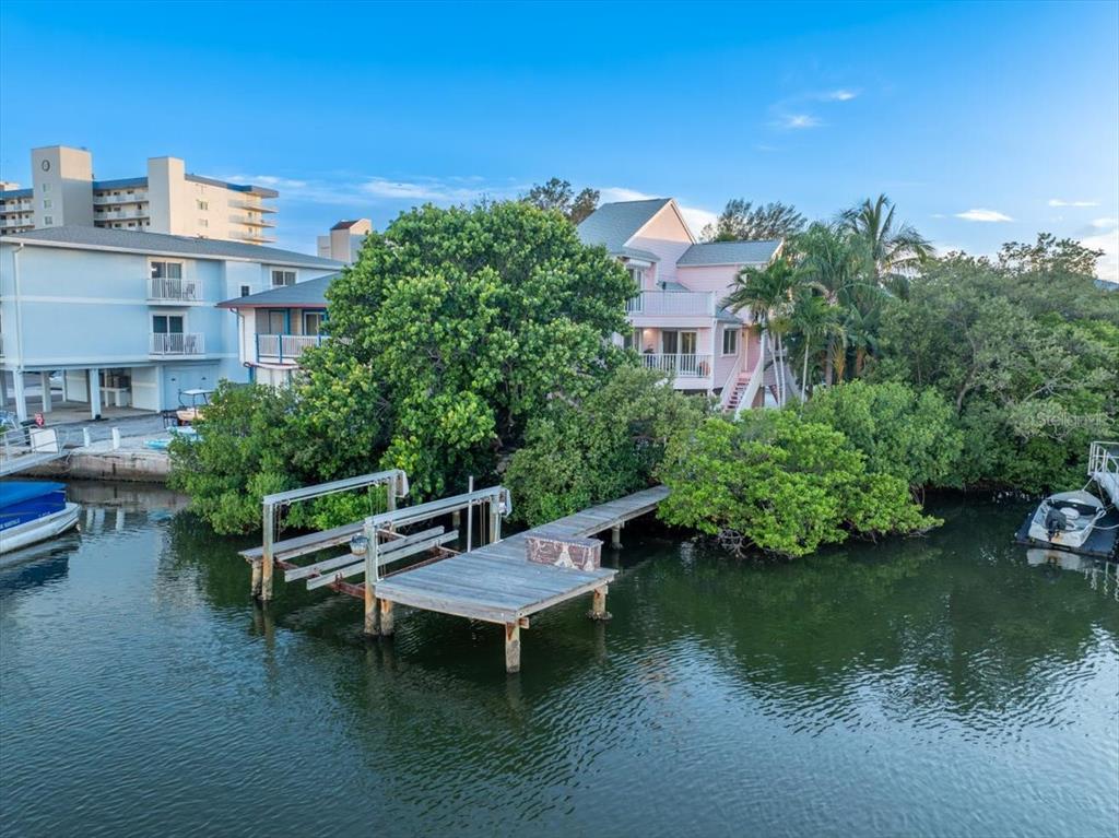 An elevated pink house sits behind a wooden dock on a calm canal — 20051 GULF BOULEVARD, INDIAN SHORES, FL