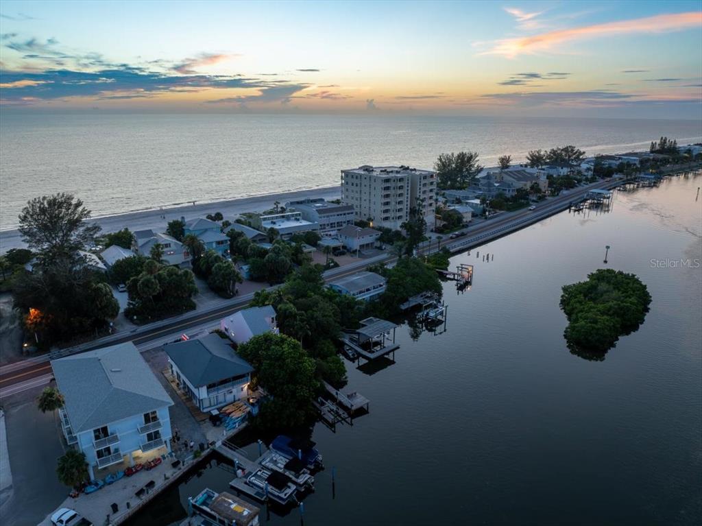 An aerial view shows a coastal neighborhood with houses, a tall building, and a waterway — 20051 GULF BOULEVARD, INDIAN SHORES, FL