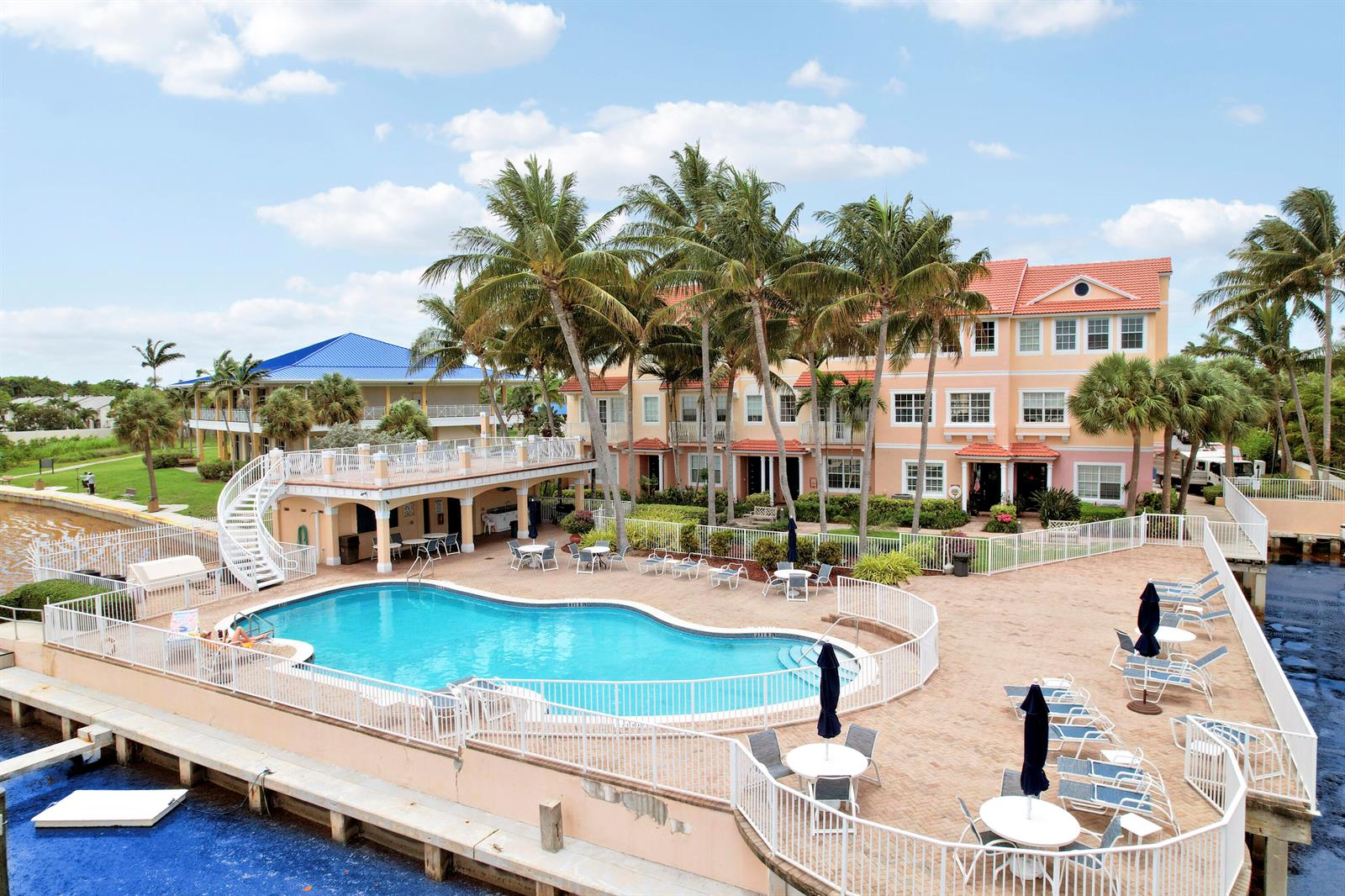 An outdoor swimming pool area with a multi-story building, palm trees, and patio furniture — 115 Harbors Way, Boynton Beach FL 33435, BOYNTON BEACH, FL