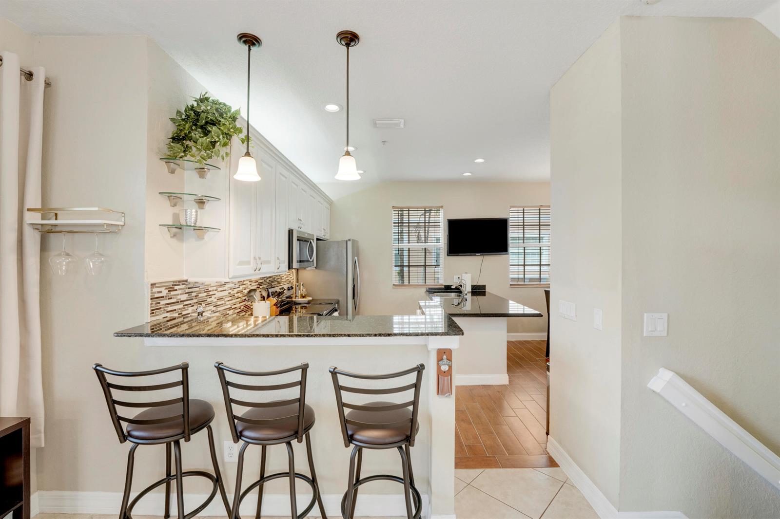 A kitchen with white cabinets, granite countertops, and three bar stools at a breakfast counter — 115 Harbors Way, Boynton Beach FL 33435, BOYNTON BEACH, FL