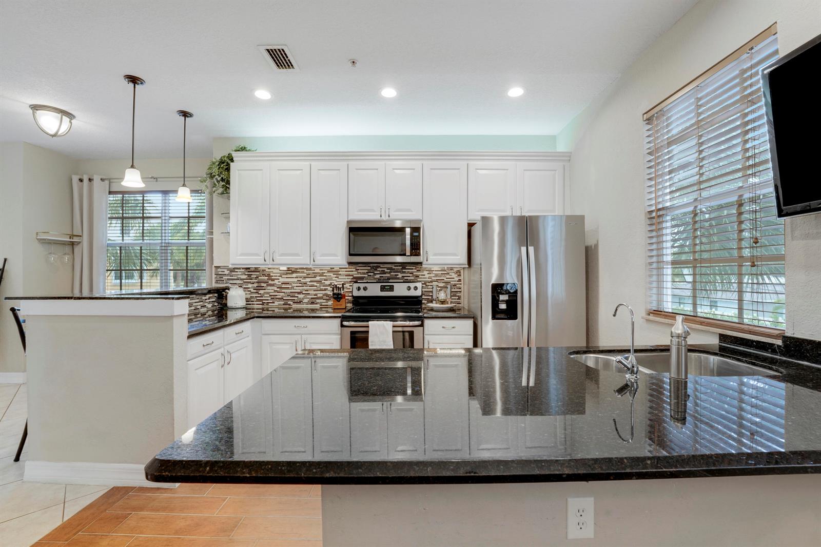 A kitchen features white cabinets, dark granite countertops, stainless steel appliances, and a breakfast bar — 115 Harbors Way, Boynton Beach FL 33435, BOYNTON BEACH, FL