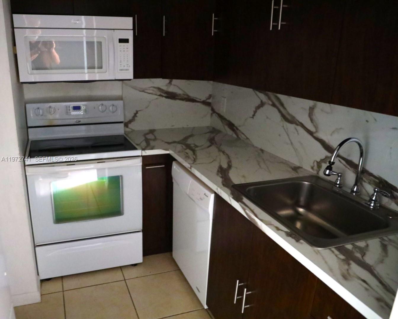 A kitchen features dark wood cabinets, white appliances, and a marble-patterned countertop and backsplash — 13714 SW 90th Ave # 25, Miami FL 33176, MIAMI, FL