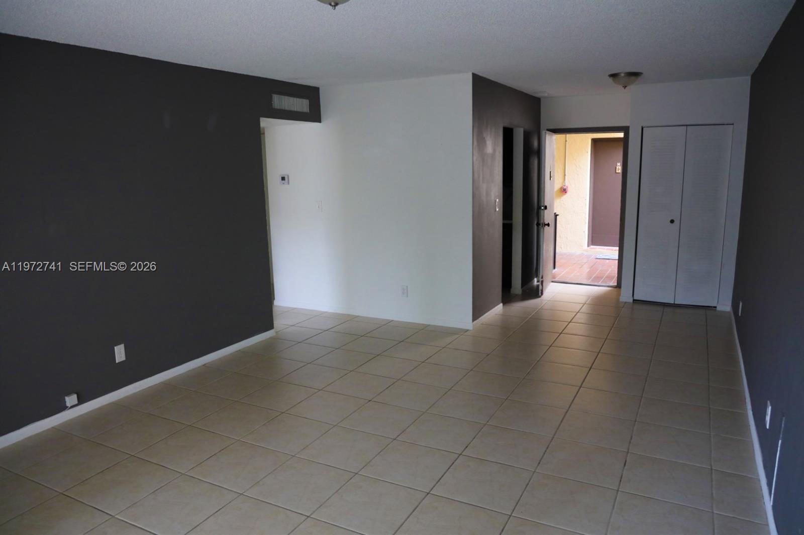 An empty room with beige tile flooring, dark accent walls, and an open exterior door — 13714 SW 90th Ave # 25, Miami FL 33176, MIAMI, FL