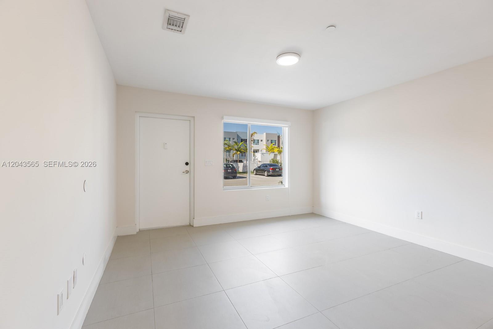 An empty room features white walls, light gray tile flooring, a window, and a door — 2505 NE 193rd St # 4108, Miami FL 33180, MIAMI, FL