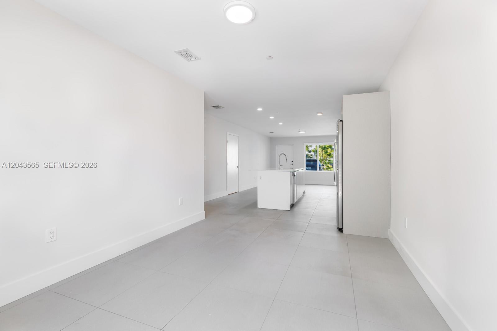 A minimalist kitchen and dining area features white walls, gray tile floors, and an island — 2505 NE 193rd St # 4108, Miami FL 33180, MIAMI, FL