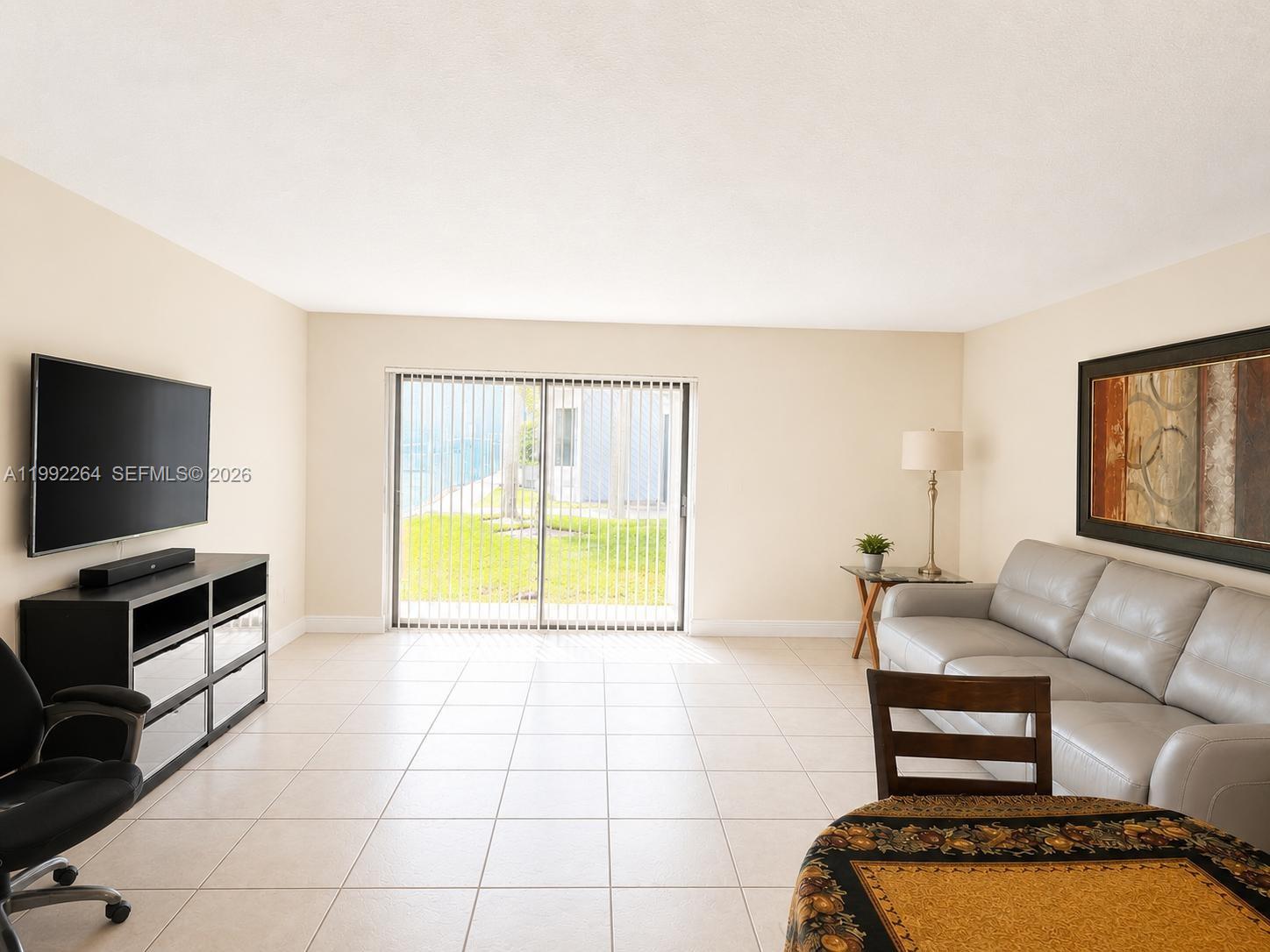 A living room features light tile floors, a grey sofa, a television, and sliding glass doors — 10060 NW 41st St # 5, Doral FL 33178, DORAL, FL