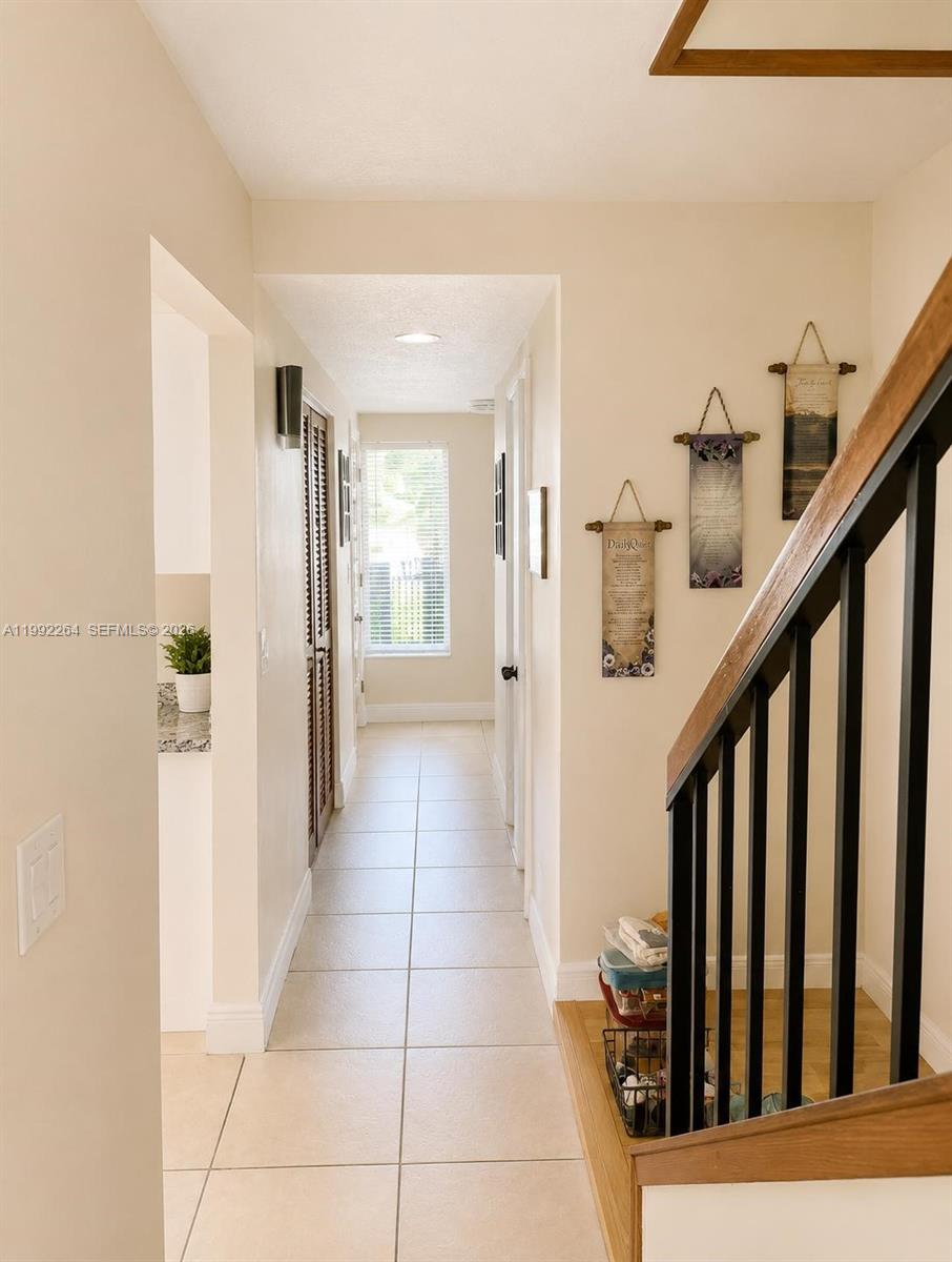 A tiled hallway leads to a windowed room, featuring a staircase with a wooden railing — 10060 NW 41st St # 5, Doral FL 33178, DORAL, FL