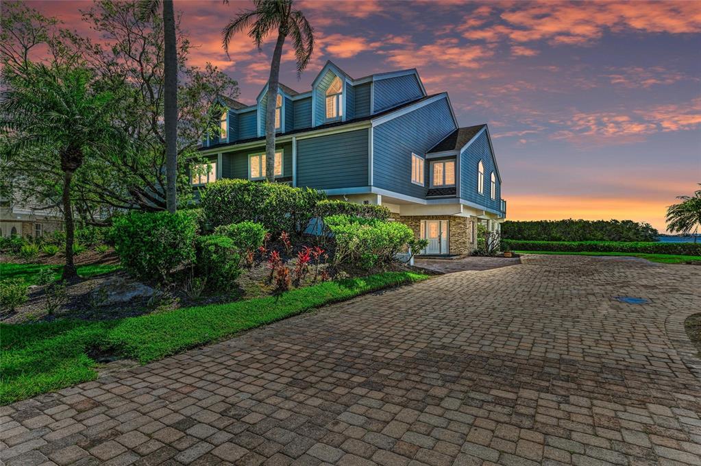 A blue multi-story house with a paved driveway and landscaped yard at sunset — 12 TIDY ISLAND BOULEVARD, BRADENTON, FL