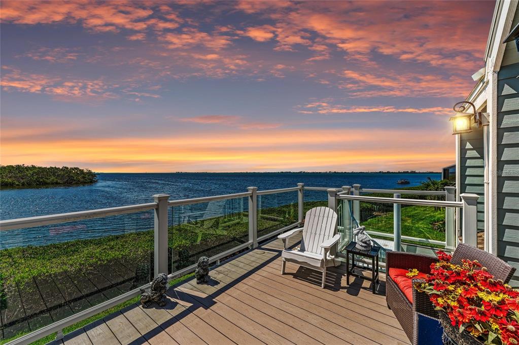 A wooden deck overlooks a bay at sunset with a white chair and outdoor furniture — 12 TIDY ISLAND BOULEVARD, BRADENTON, FL