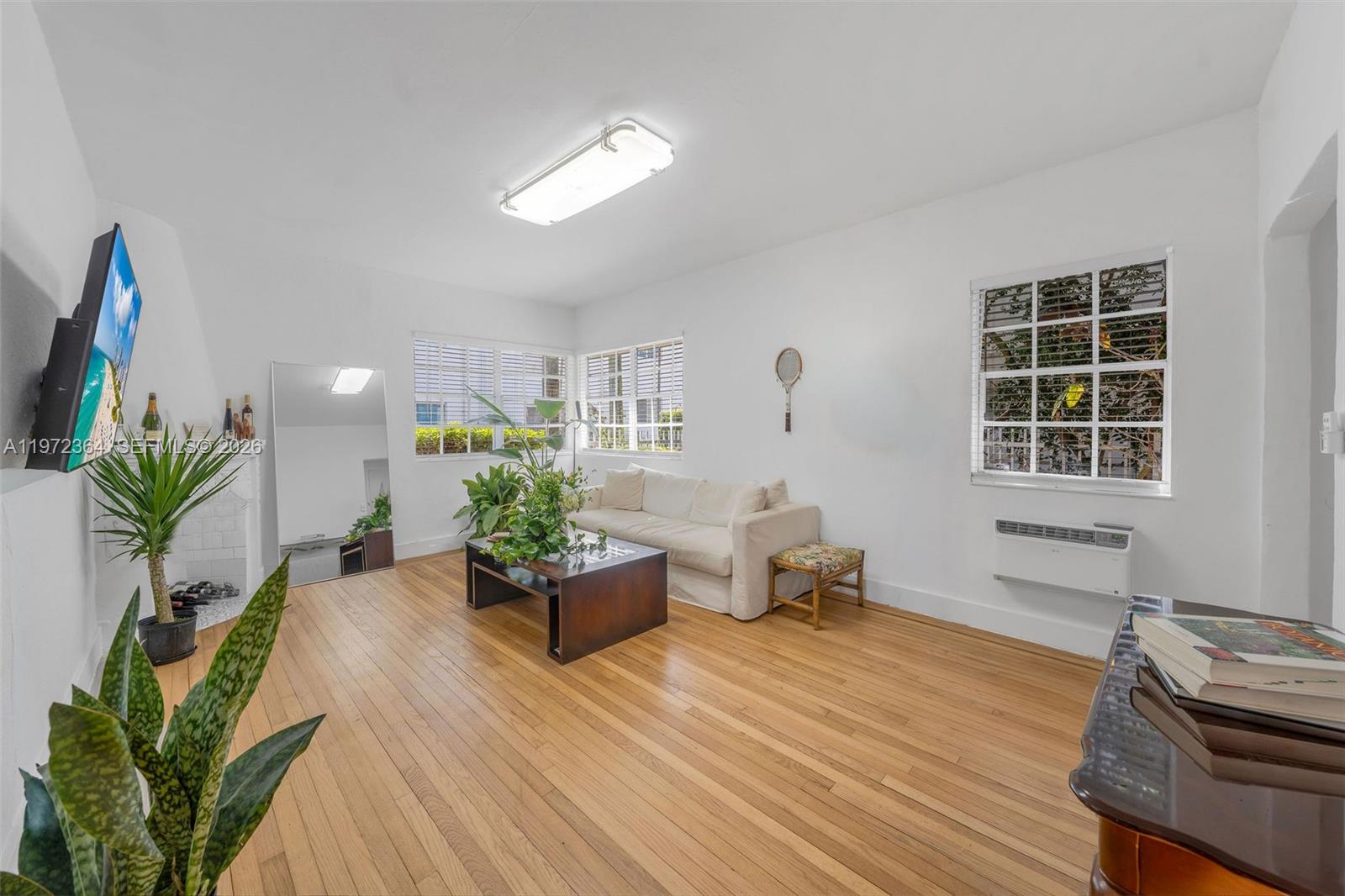 A living room features white walls, hardwood floors, a sofa, and a wall-mounted television — 1309 Euclid Ave # 6, Miami Beach FL 33139, MIAMI BEACH, FL