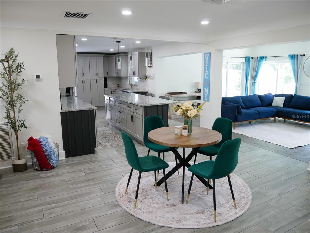 An open-concept kitchen and dining area features gray cabinetry, a kitchen island, and green chairs — 8280 32ND AVENUE N, ST PETERSBURG, FL