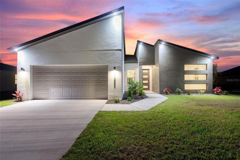 A modern single-story house with a two-car garage, gray stucco facade, and a sunset sky — 24399 SW KINGSWAY CIRCLE, ARCADIA, FL