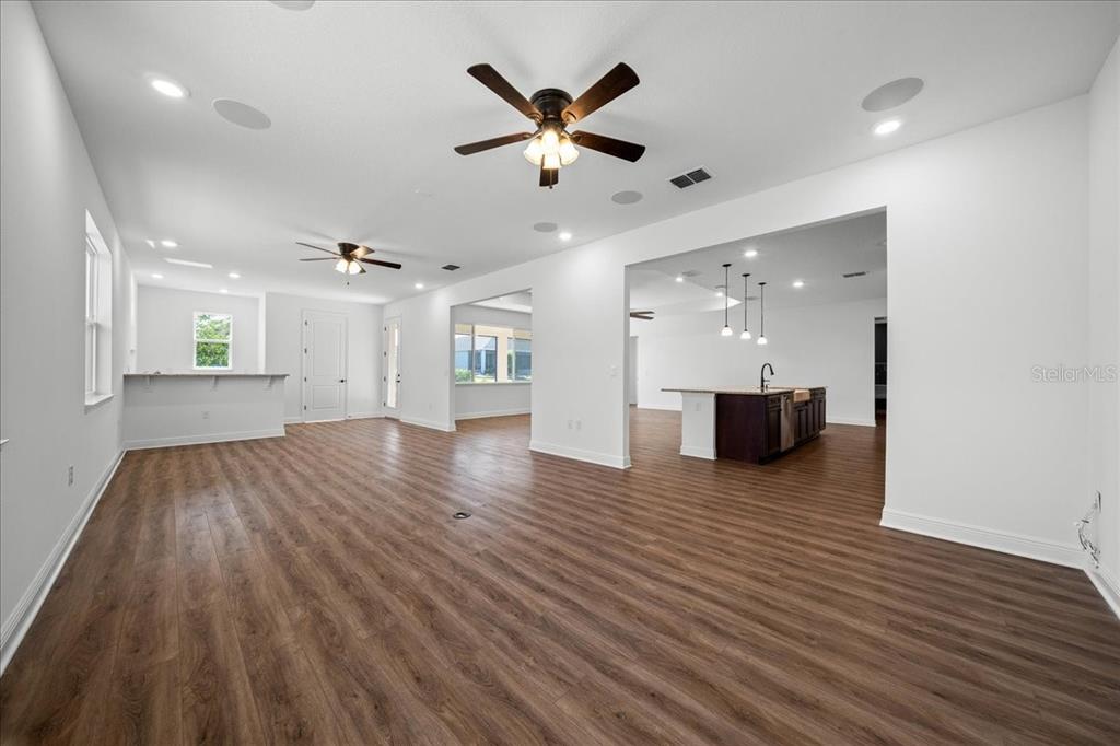 A spacious, open-concept living area features wood-look flooring, white walls, and two ceiling fans — 8233 SW 93RD TERRACE, OCALA, FL