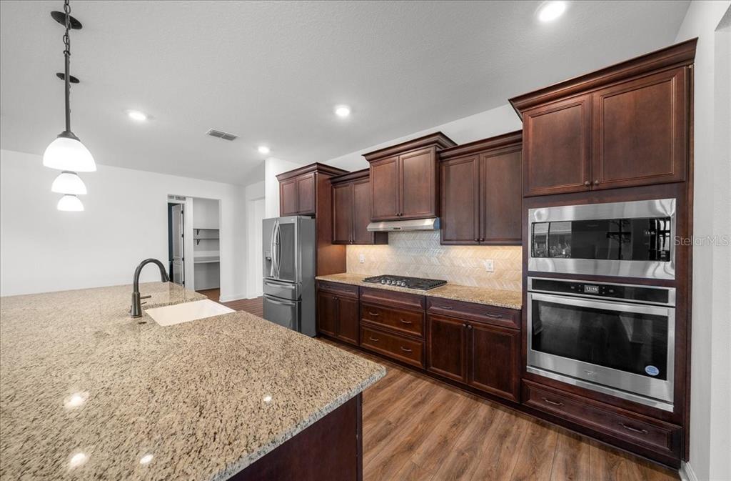 A kitchen featuring dark wood cabinets, granite countertops, stainless steel appliances, and a large island — 8233 SW 93RD TERRACE, OCALA, FL