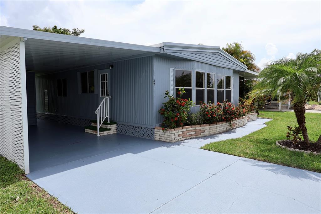 A light blue mobile home features a carport, a brick planter, and a palm tree — 25163 MARION AVENUE UNIT 47, PUNTA GORDA, FL
