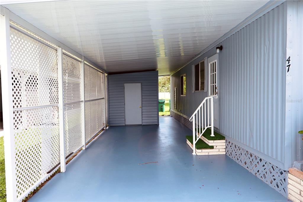 A covered carport with a blue floor, lattice side wall, and stairs leading to a door — 25163 MARION AVENUE UNIT 47, PUNTA GORDA, FL