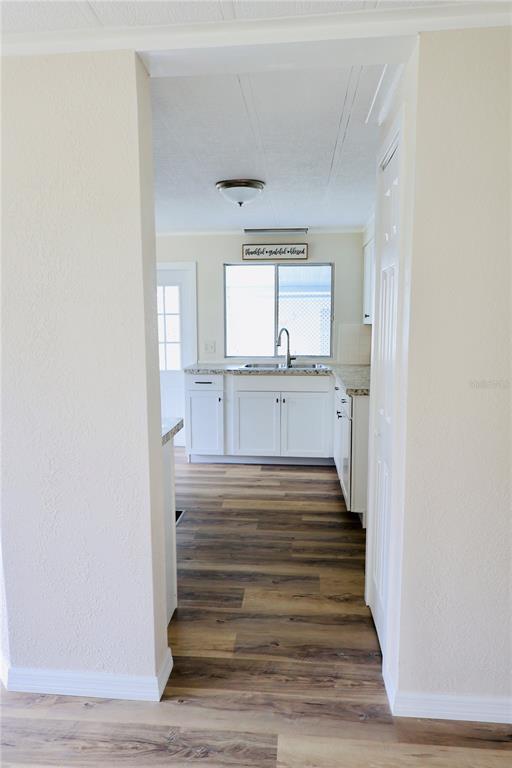 A view through a doorway into a kitchen with white cabinets and wood-look flooring — 25163 MARION AVENUE UNIT 47, PUNTA GORDA, FL