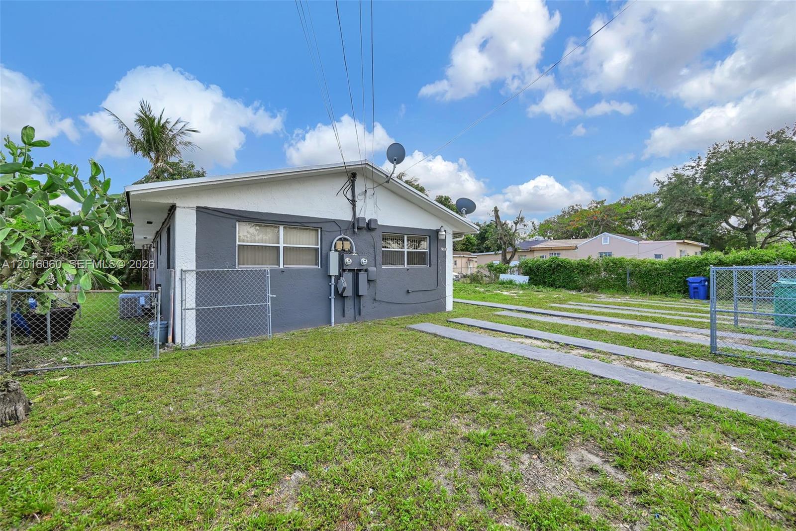 The exterior of a gray house features a chain-link fence and a concrete driveway — 2352 NW 102nd St, Miami FL 33147, MIAMI, FL