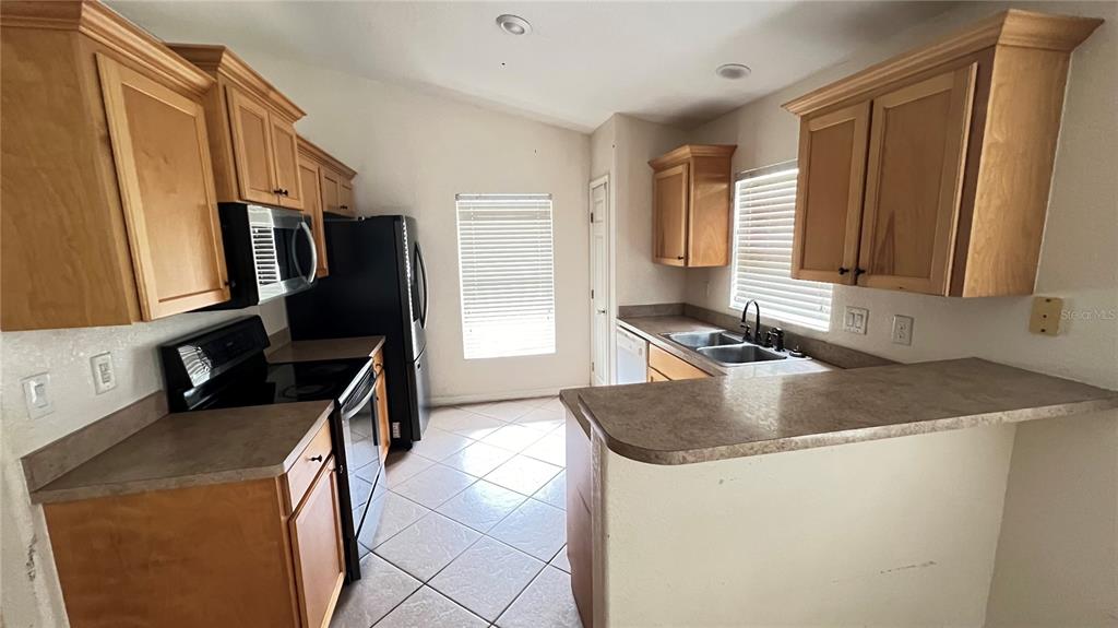 A kitchen features light wood cabinets, laminate countertops, a black refrigerator, and tile flooring — 513 LEMON STREET, AUBURNDALE, FL