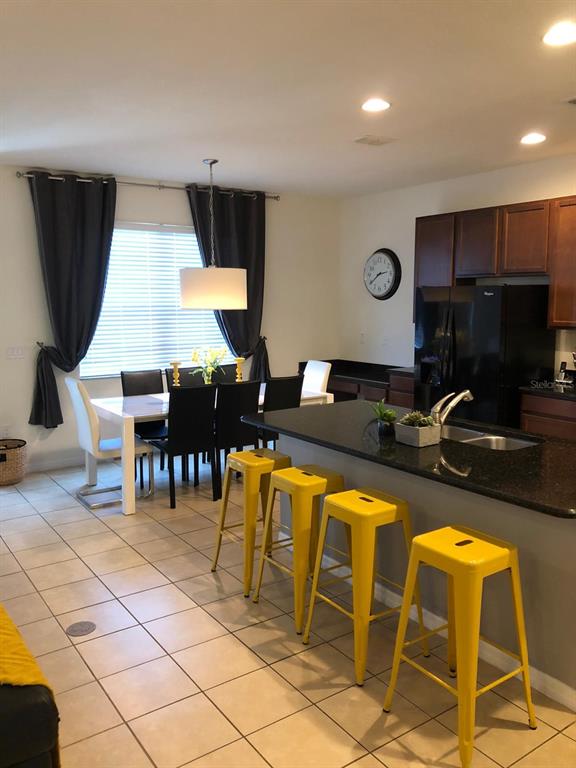 A kitchen with a dark granite island and yellow stools next to a dining area — 921 LAS FUENTES DRIVE, KISSIMMEE, FL