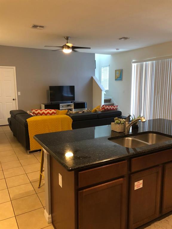 A kitchen island with a dark countertop overlooks a living room with a sectional sofa — 921 LAS FUENTES DRIVE, KISSIMMEE, FL