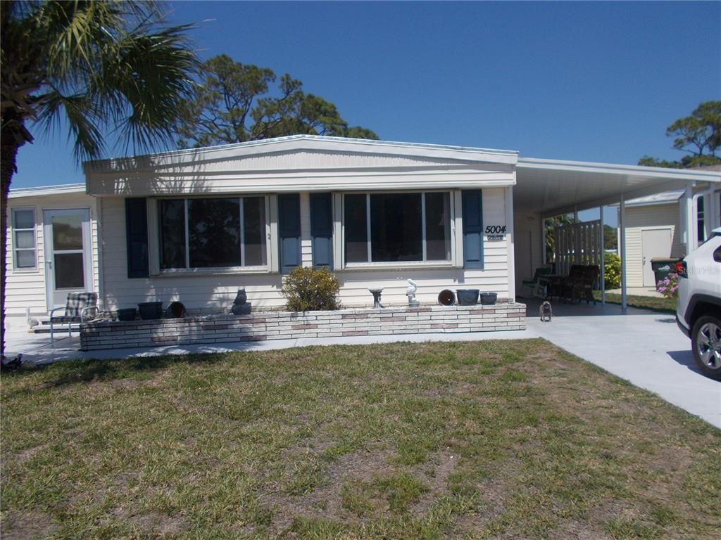 A single-story manufactured home with a carport, brick planter, and blue shutters — 5004 PALENA BOULEVARD, NORTH PORT, FL
