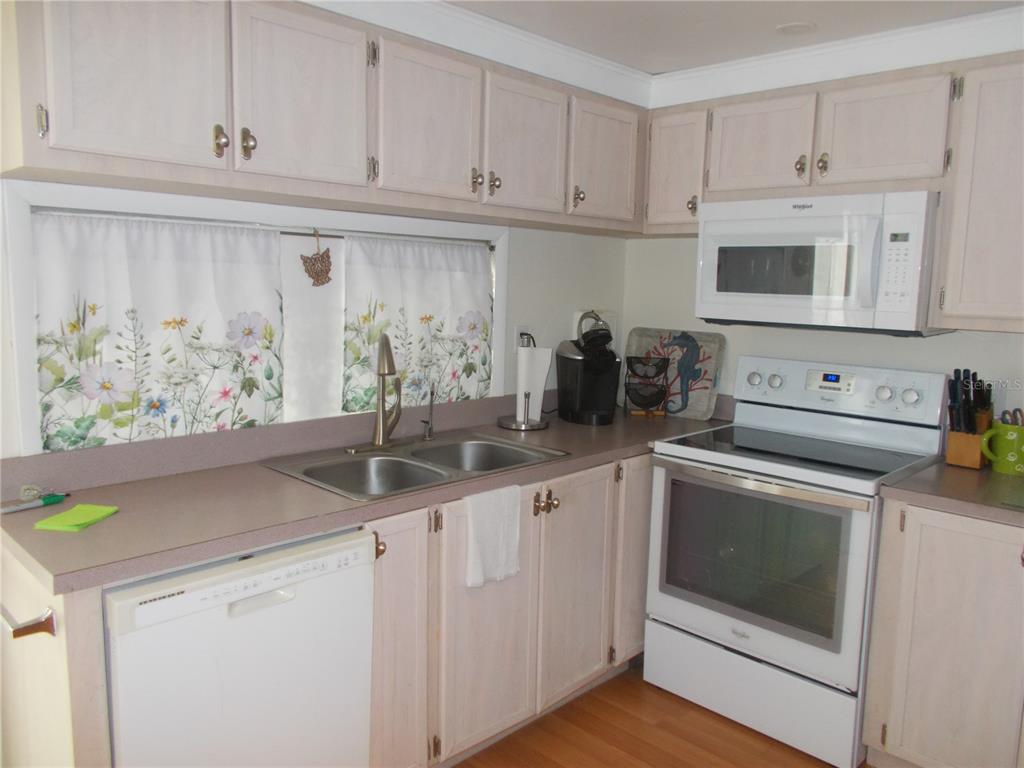 A kitchen features light wood cabinets, white appliances, a double sink, and floral curtains — 5004 PALENA BOULEVARD, NORTH PORT, FL